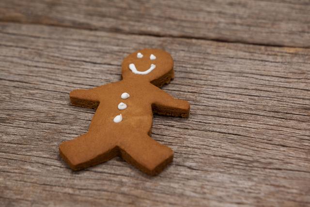 Gingerbread man cookie with white icing details lying on a rustic wooden surface. Ideal for holiday-themed designs, Christmas cards, festive advertisements, baking blogs, and culinary magazines.