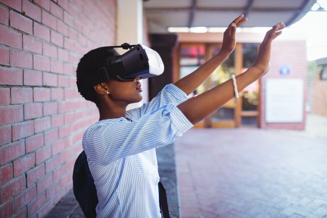 Young schoolgirl using virtual reality headset on school campus, exploring digital and immersive experiences. Ideal for educational technology, modern learning environments, and innovation in education.