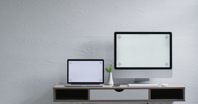 Modern workspace featuring a laptop and desktop computer placed on a minimalist desk with a small plant for subtle decoration. The image is ideal for illustrating home office setups, technology-focused work environments, or modern minimalist design principles. Suitable for blog posts about productivity, office ergonomics, or interior design trends.