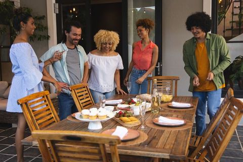 Multiracial friends gathering outdoors around wooden table sharing cupcakes and wine