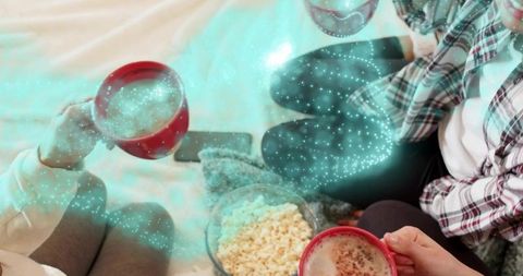 Friends sharing cozy movie night sipping hot drinks and popcorn on bed with red mugs
