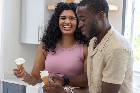Smiling multicultural couple enjoying ice cream together in sunlit modern kitchen