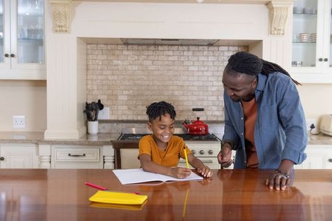 African american father helping son with homework on kitchen island, smiling together