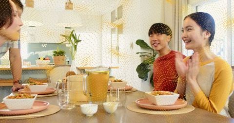 Sunlit family gathering around modern dining table with pitcher, pink plates, indoor plants and cera