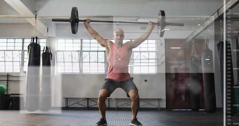 Fit man performing overhead squat with barbell in bright gym for strength and core power
