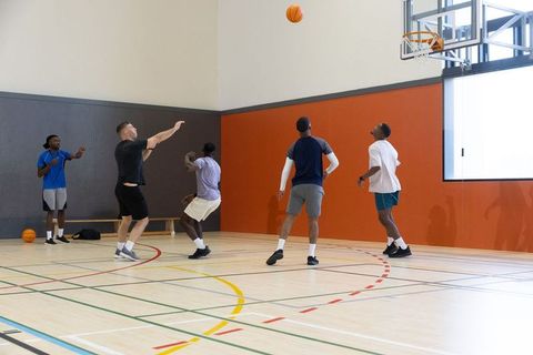 Multiracial young men playing basketball indoors, celebrating jump shot on gym court