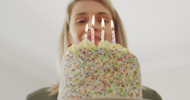 Smiling caucasian woman with birthday cake and four lit candles, unaltered. Birthday, party and celebration concept.