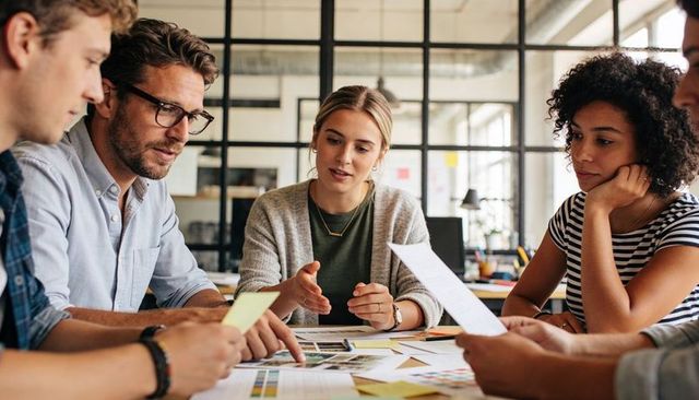 Cardigan-wearing leader guiding diverse team through collaborative design brainstorming