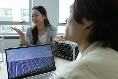 Women presenting solar and wind energy solutions on laptop during collaborative meeting