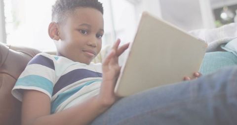 Relaxing young boy using tablet on sofa at home, studying and playing in sunlit room
