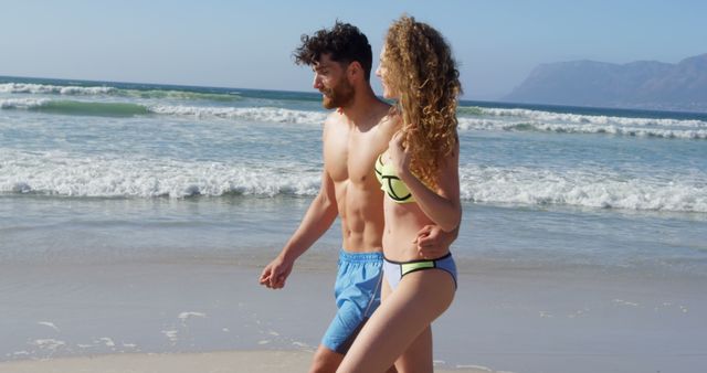Couple spending quality time walking arm in arm on sandy beach with gentle waves lapping the shore. Ideal for campaigns promoting summer vacations, beach destinations, romantic getaways, and leisure activities.