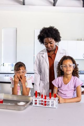 Black stem teacher guiding two young girls conducting colorful test tube chemistry