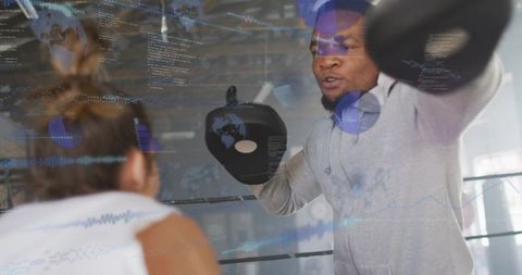 Coach holding focus mitts, trainee punching in boxing ring with fitness data overlay