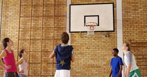 Students practicing basketball under hoop in brick gymnasium, teamwork and youth sports
