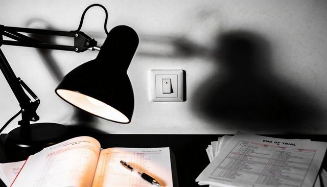 Desk lamp casting dramatic shadow over open textbook with pen and end-of-trial papers