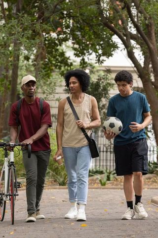 African american men walking park path carrying soccer ball and bicycle, urban leisure