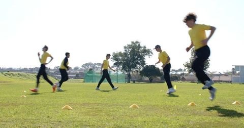 Diverse male team sprinting across grass field in cone drill building speed, coordination