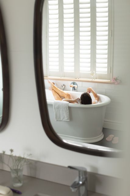 Reflection of woman in mirror taking bath in bathtub at bathroom