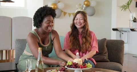 Cheerful Lesbians Celebrating Birthday with Cake and Candles on Couch