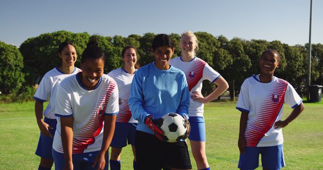 Team of diverse female football players standing with ball and smiling on sunny sports field. Active lifestyle, sport, competition, hobby and wellbeing, unaltered.