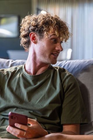 Young man on sofa holding smartphone and looking sideways in relaxed living room