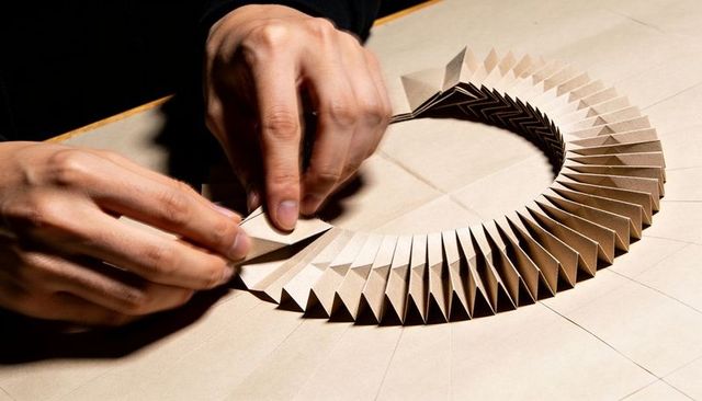 Crafting geometric kraft paper ring, hands folding pleats and aligning origami circle