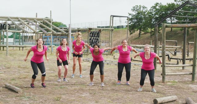 Group of women performing exercises at an outdoor obstacle course, showing teamwork and unity. All women are wearing coordinated pink shirts and appear actively engaged in fitness and training. This image is ideal for content related to group fitness, outdoor activities, health and wellness, or teamwork exercises. Perfect for articles on healthy living, team building, and adventure challenges.