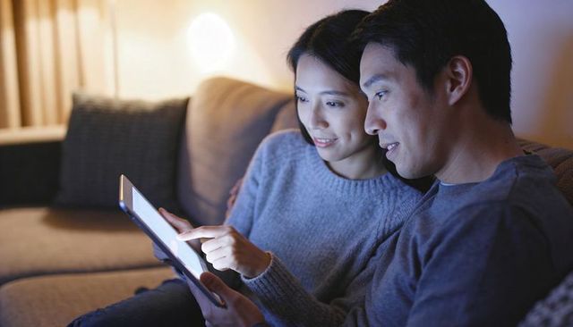 Couple relaxing on sofa using tablet together at night warm cozy living room ambience