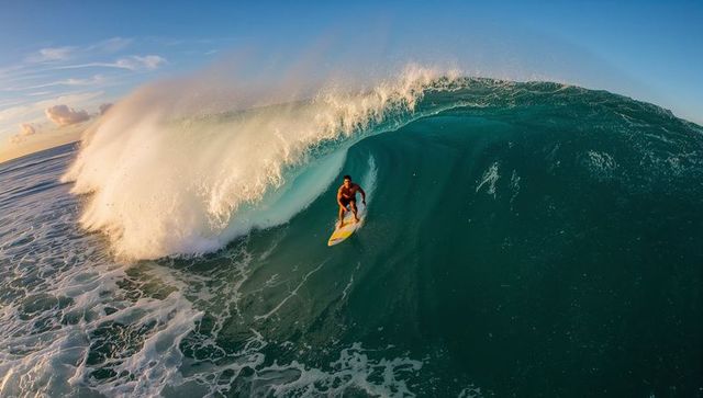 Surfer riding inside giant turquoise barrel wave at golden sunrise, dramatic ocean action