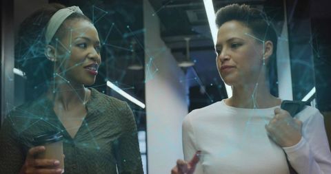 Two Businesswomen Discussing Data Visualization While Walking Through Modern Tech Office