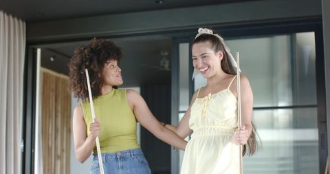 Two diverse women playing pool and laughing in contemporary living room with glass doors