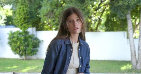 Young woman standing in sunlit backyard wearing denim jacket and casual summer outfit