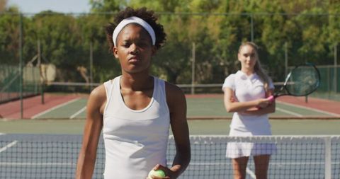 Focused young tennis player preparing serve on outdoor court with teammate in background