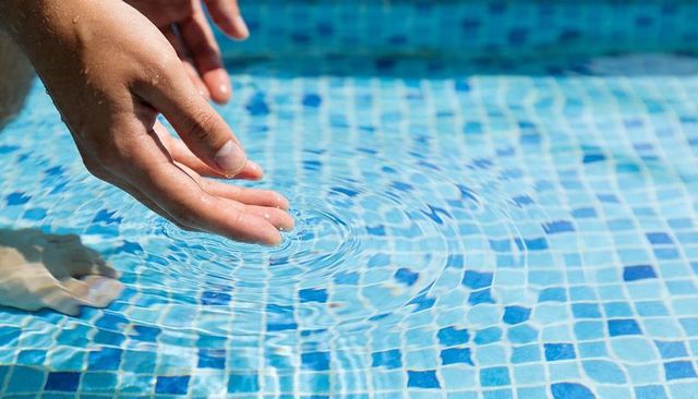 Hands skimming pool water creating concentric ripples over blue mosaic tiles