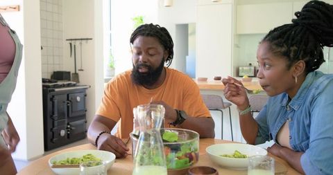 African family enjoying fresh salad at kitchen table, casual home meal with natural light