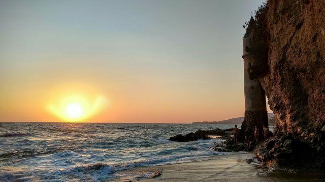 Scenic sunset by a castle tower on a rocky beach, with waves gently hitting the shore. Ideal for use in travel brochures, websites, and inspirational posters emphasizing nature's beauty and tranquility.