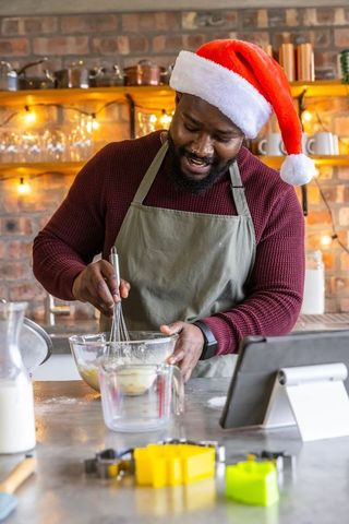 African american man wearing santa hat baking holiday cookies in rustic kitchen
