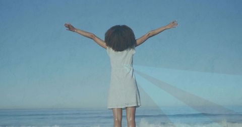 Woman embracing ocean breeze in white dress by beach
