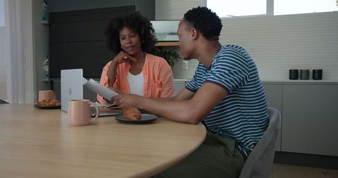 Young couple collaborating at kitchen table with laptop and snacks