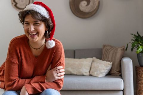 Laughing woman wearing santa hat on cozy sofa celebrating casual home holiday cheer