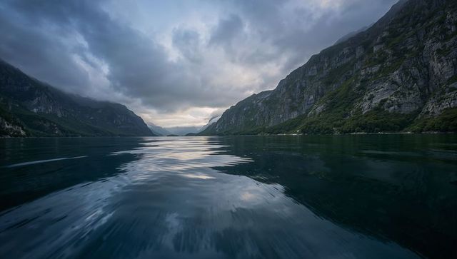 Moody alpine panoramic lake reflecting dawn light between granite cliffs in remote valley