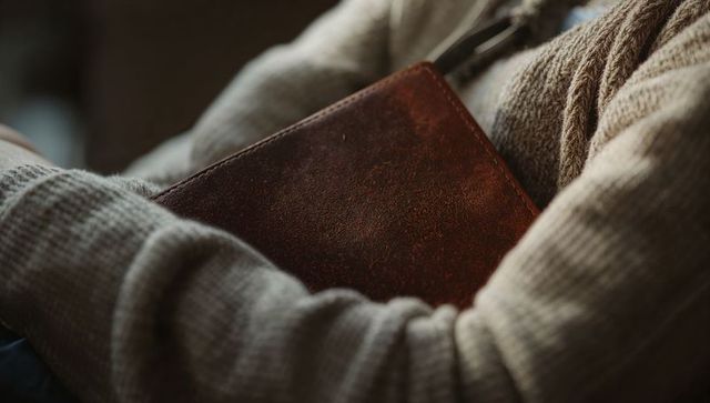 Cradling vintage leather journal while wearing cozy beige knit sweater and scarf