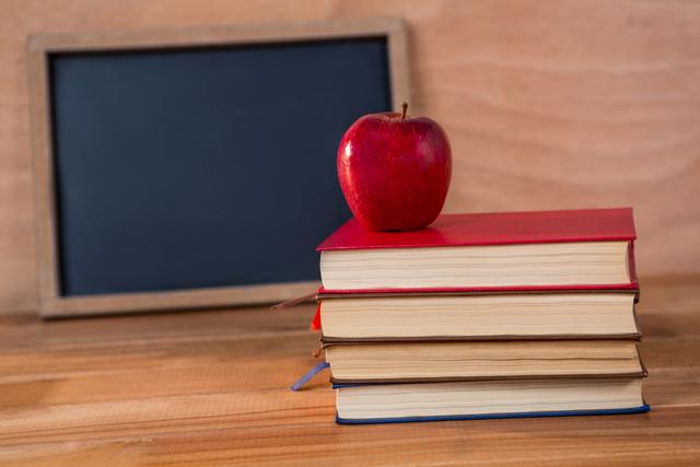 Close-up of books stack with red apple on a table