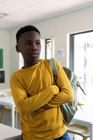 African american teen standing in classroom carrying backpack and looking thoughtful