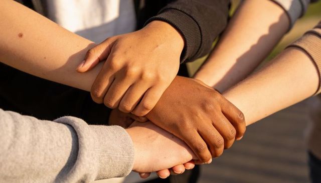 Multiracial hands joining in circle showing unity trust teamwork friendship outdoors