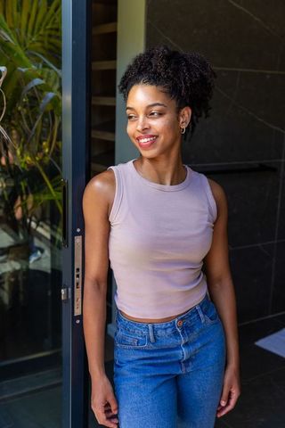 African american woman leaning and smiling in modern doorway wearing tank top and jeans
