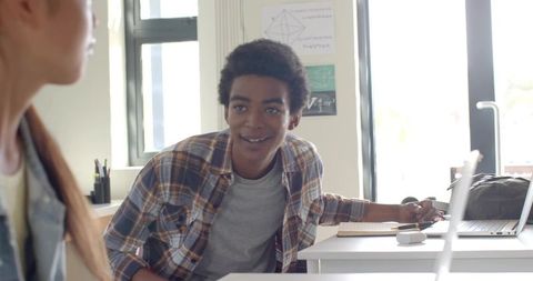 Young student leaning forward reaching for laptop during collaborative classroom study