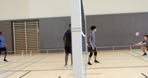 Multiracial male volleyball team practicing indoor court drills, passing, digging, teamwork