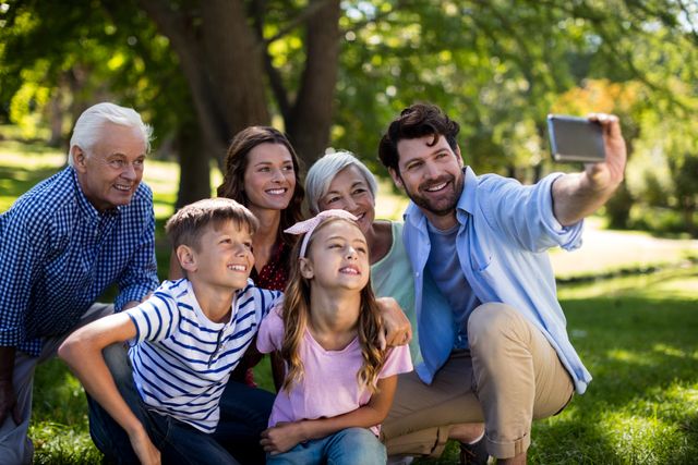Multi-generational family enjoying time together in a park, capturing a happy moment with a selfie. Ideal for use in advertisements, family-oriented content, social media campaigns, and articles about family bonding, outdoor activities, and creating memories.