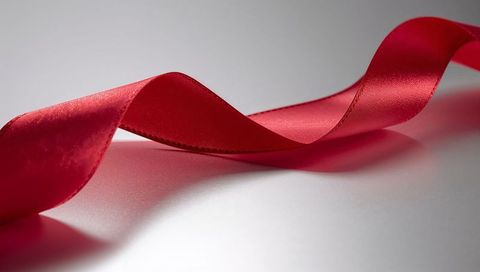 Flowing red satin ribbon with stitched edge and glossy reflection on pale tabletop